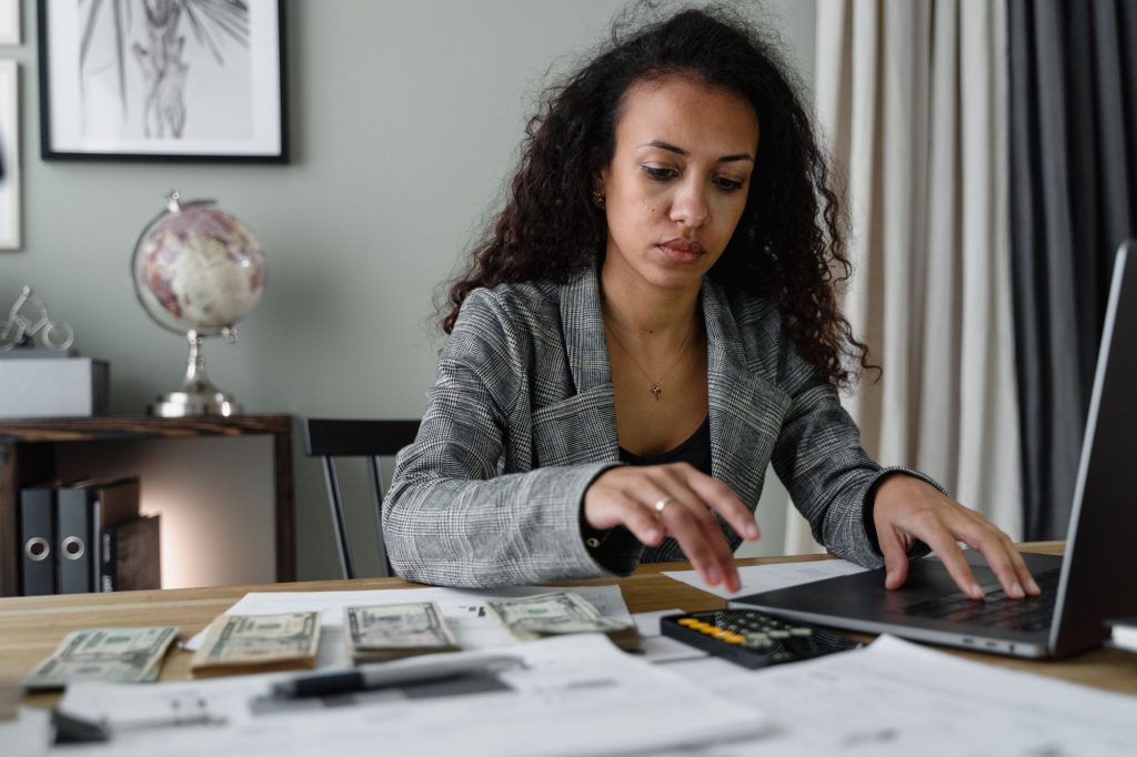 A woman reviewing her finances at her desk with a laptop and phone