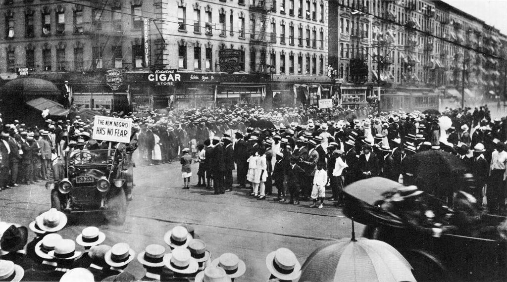 Crowds in straw boaters line Lenox Avenue at 135th Street in Harlem during a 1920 parade